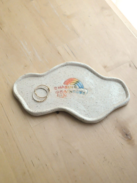 White specked trinket dish with a rainbow design, displayed with rings on a wooden surface