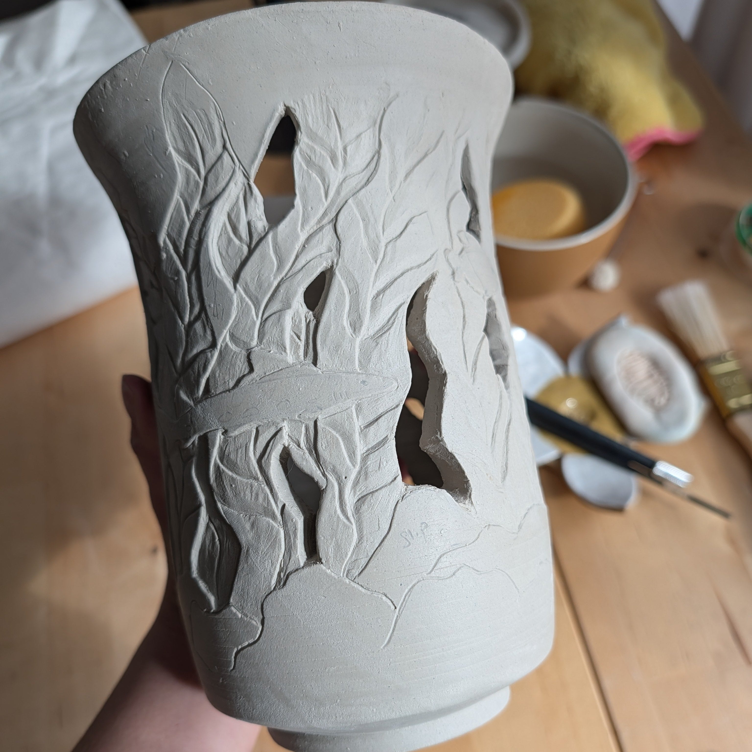 Ceramic vase with kelp forest design held by a person over a wooden table.