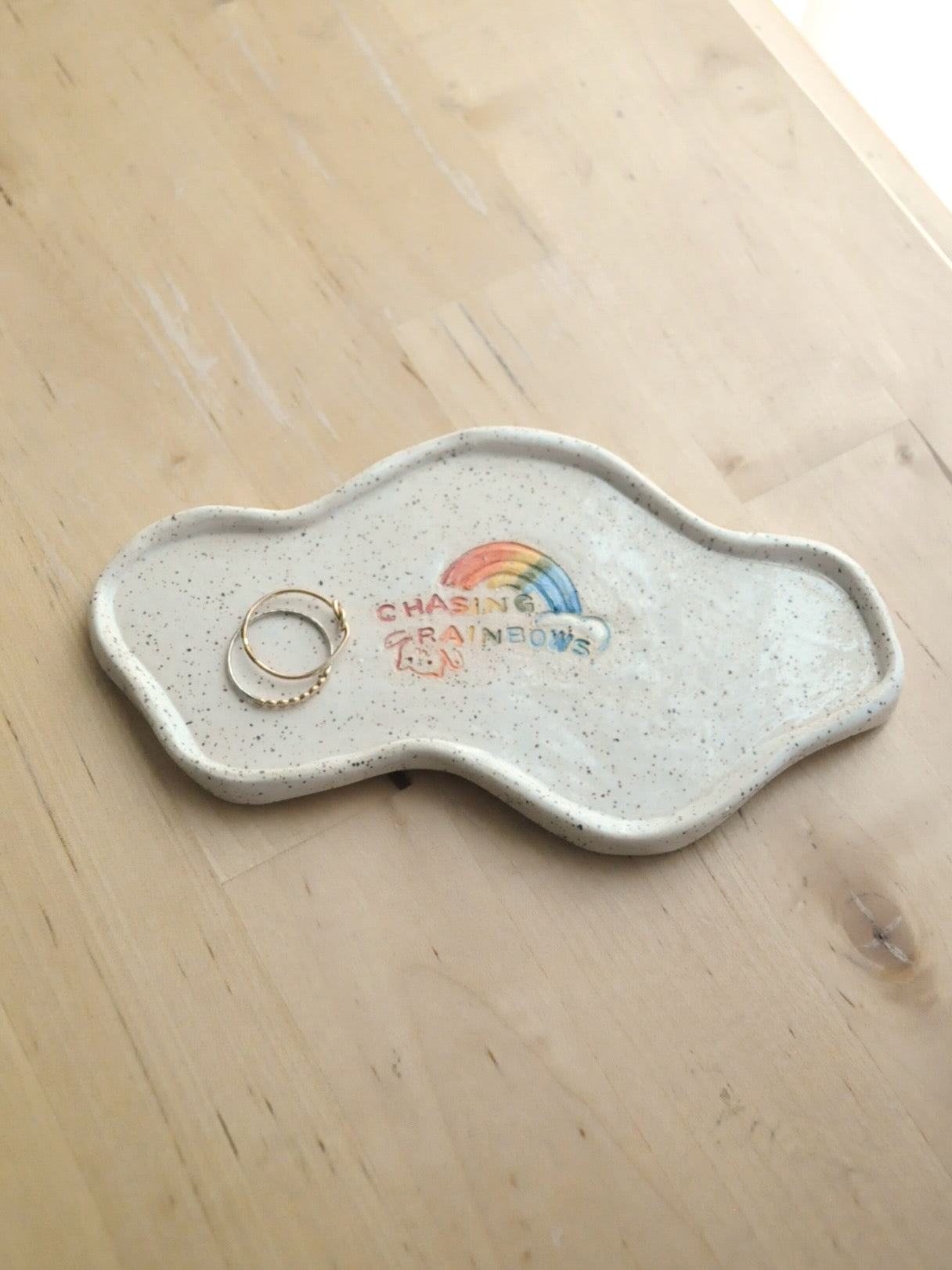 White specked trinket dish with a rainbow design, displayed with rings on a wooden surface