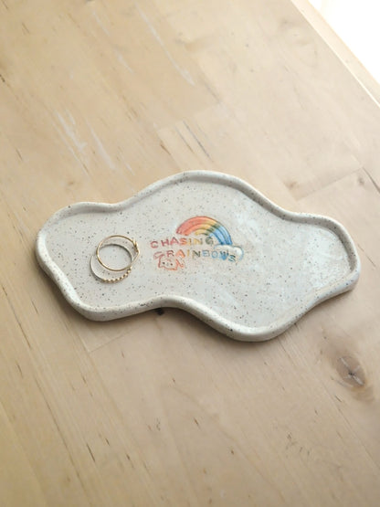 White specked trinket dish with a rainbow design, displayed with rings on a wooden surface