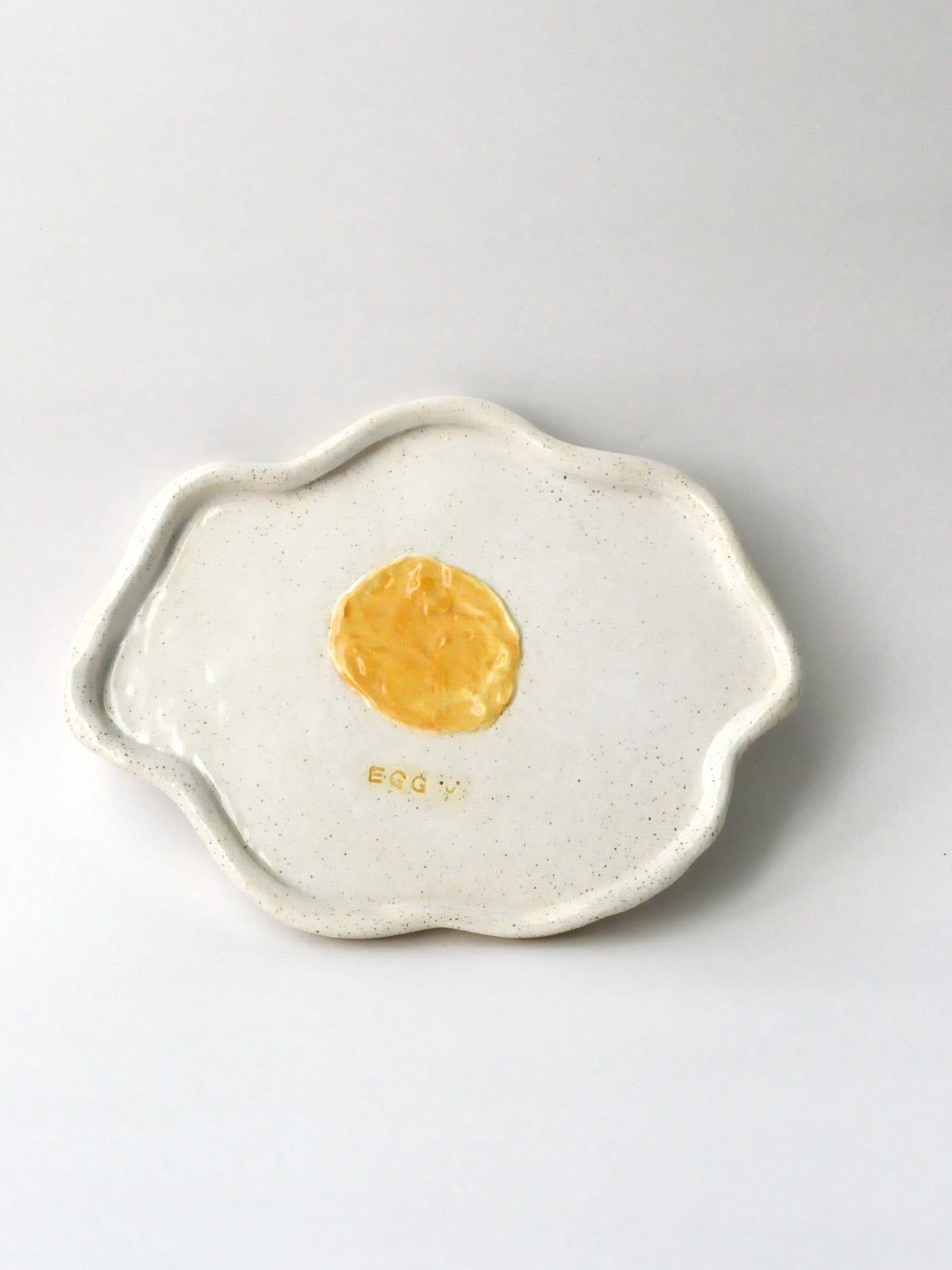 Ceramic plate shaped like a fried egg with a yellow center on a white background