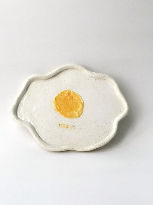 Ceramic plate shaped like a fried egg with a yellow center on a white background
