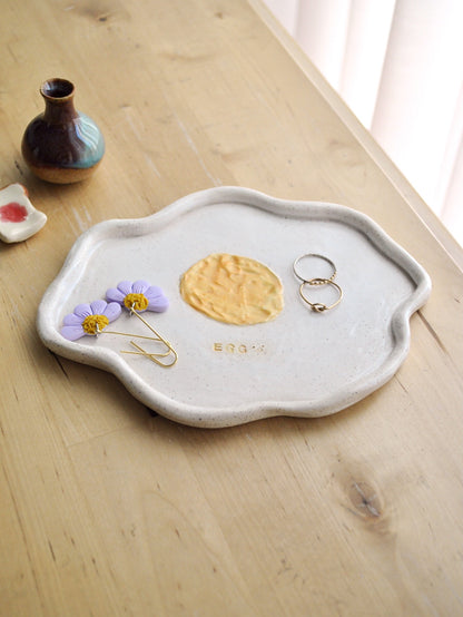 Ceramic plate shaped like a fried egg with a yellow center displayed on a wooden surface.