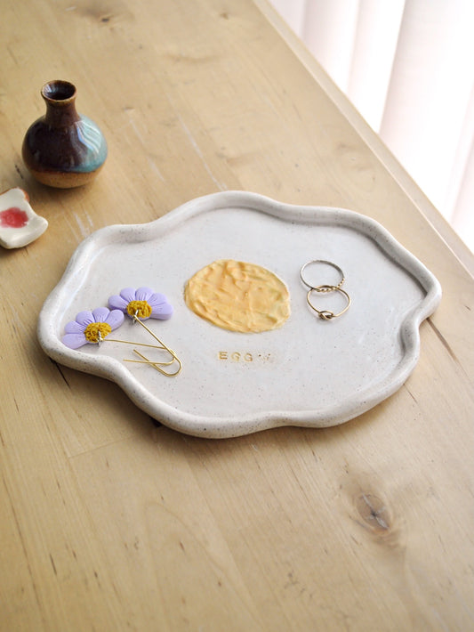 Ceramic plate shaped like a fried egg with a yellow center displayed on a wooden surface.