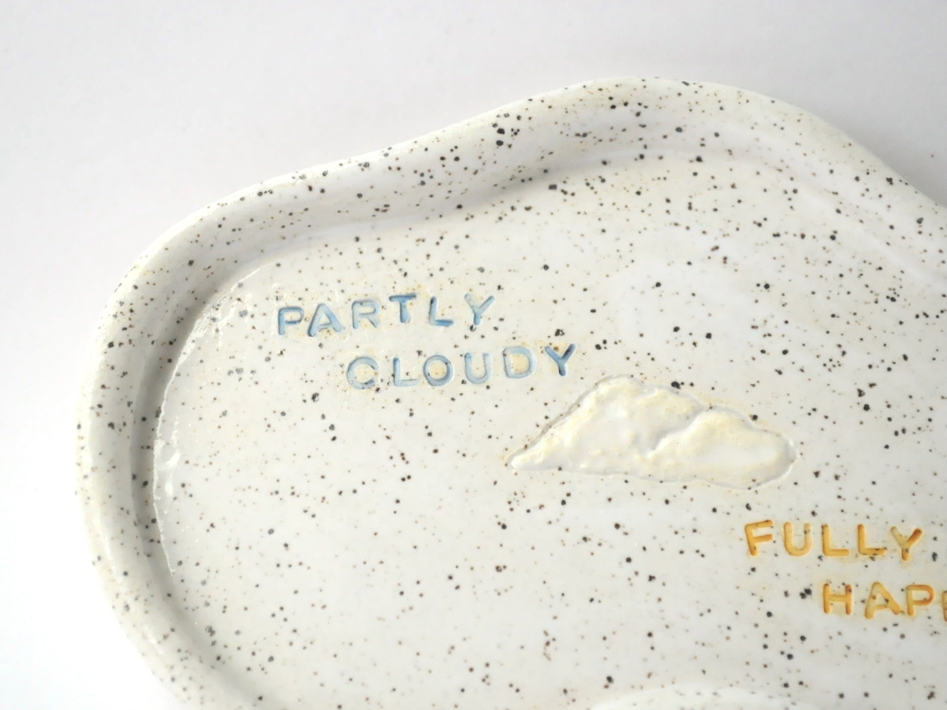 Speckled ceramic plate with cloud design and text on a white background