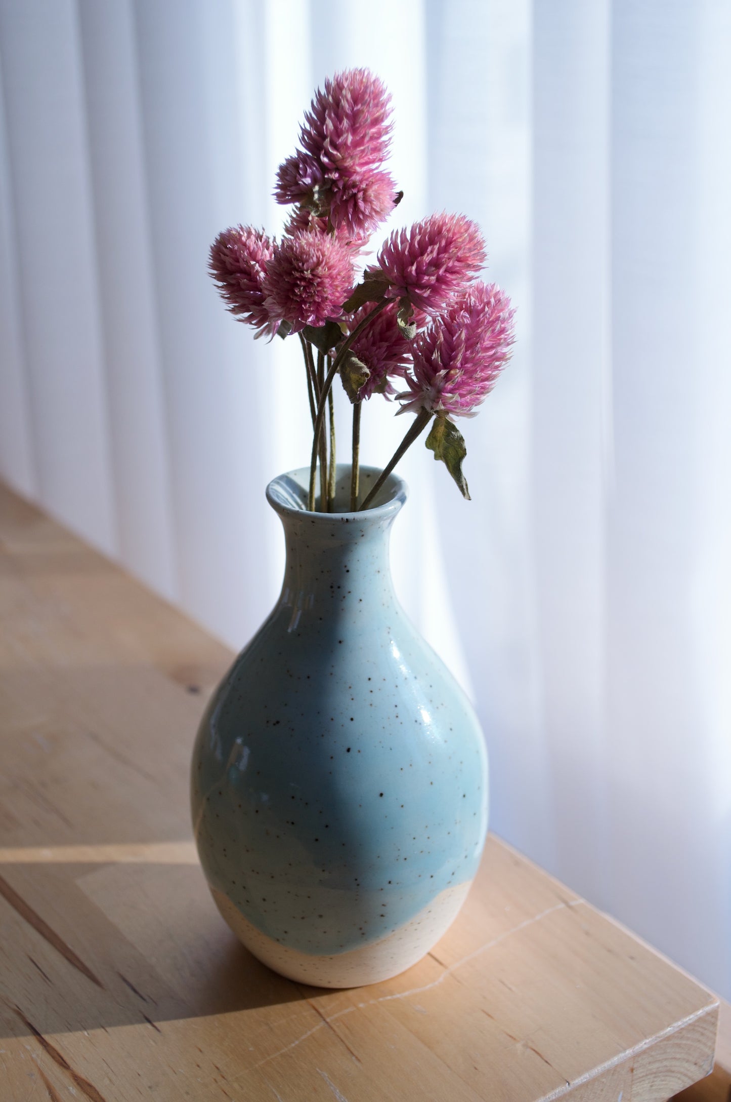 Blue speckled vase with pink flowers on a wooden surface