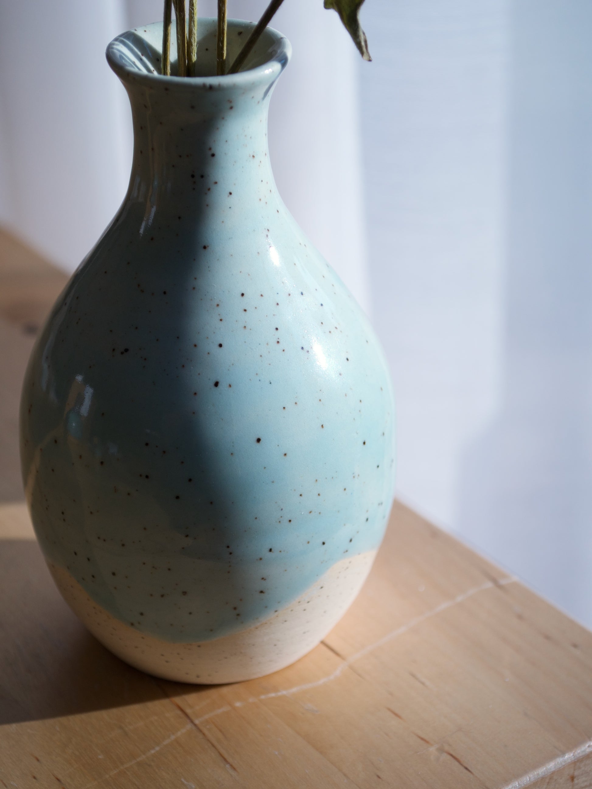 Speckled blue ceramic vase on a wooden surface with a white background