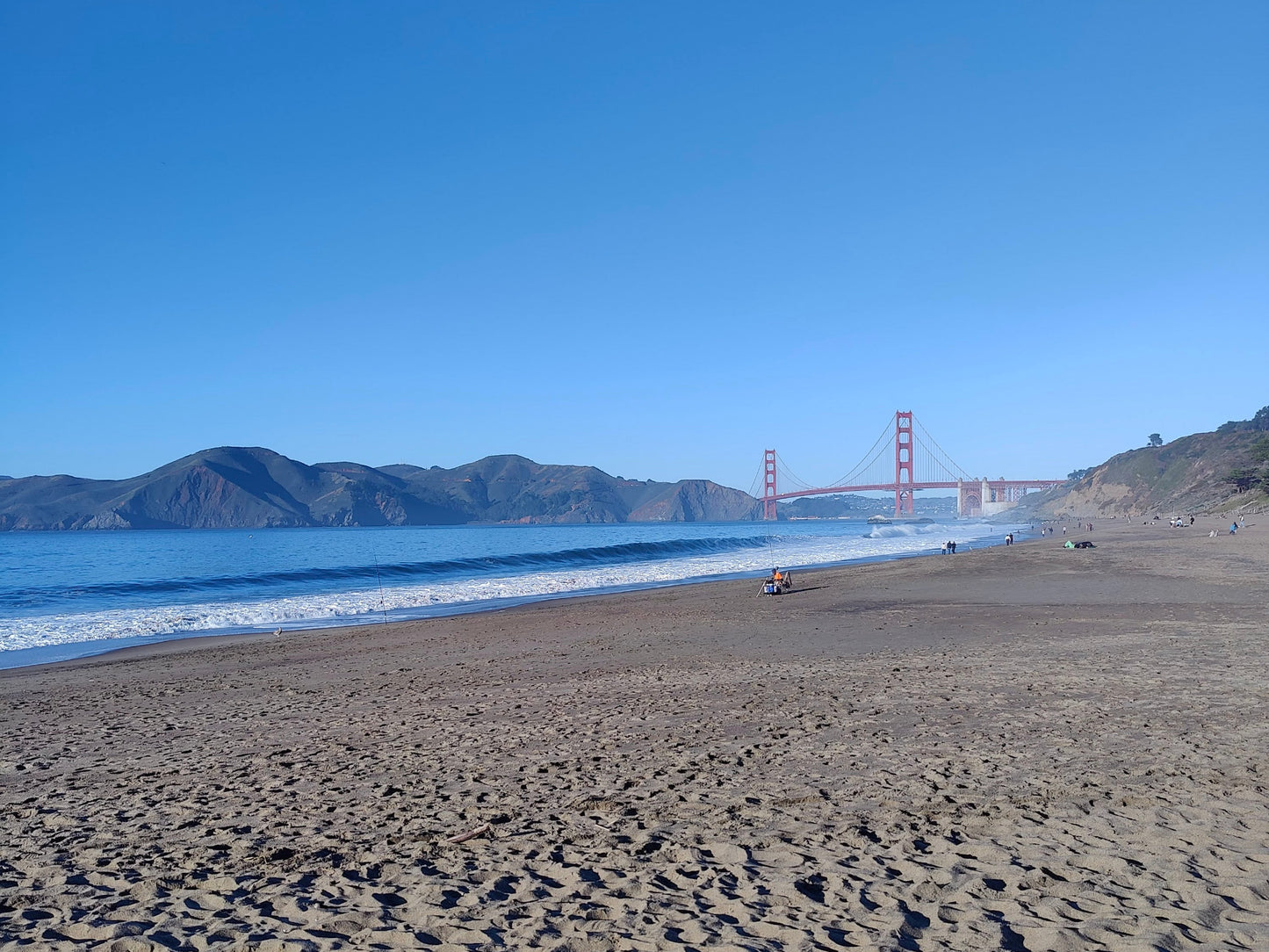 Baker Beach with the Golden Gate Bridge in the distance under a clear blue sky.