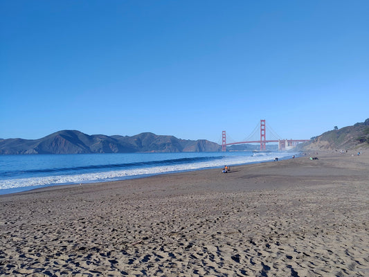 Baker Beach with the Golden Gate Bridge in the distance under a clear blue sky.